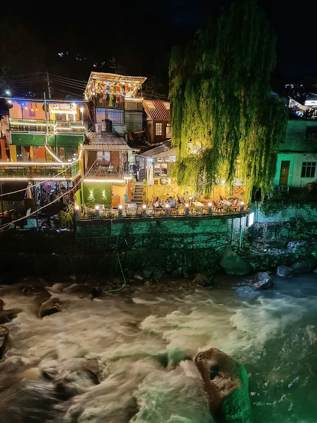 A night market strung with lights beside a stream near Manali